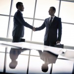 Silhouettes of two businessmen standing by the window and handshaking